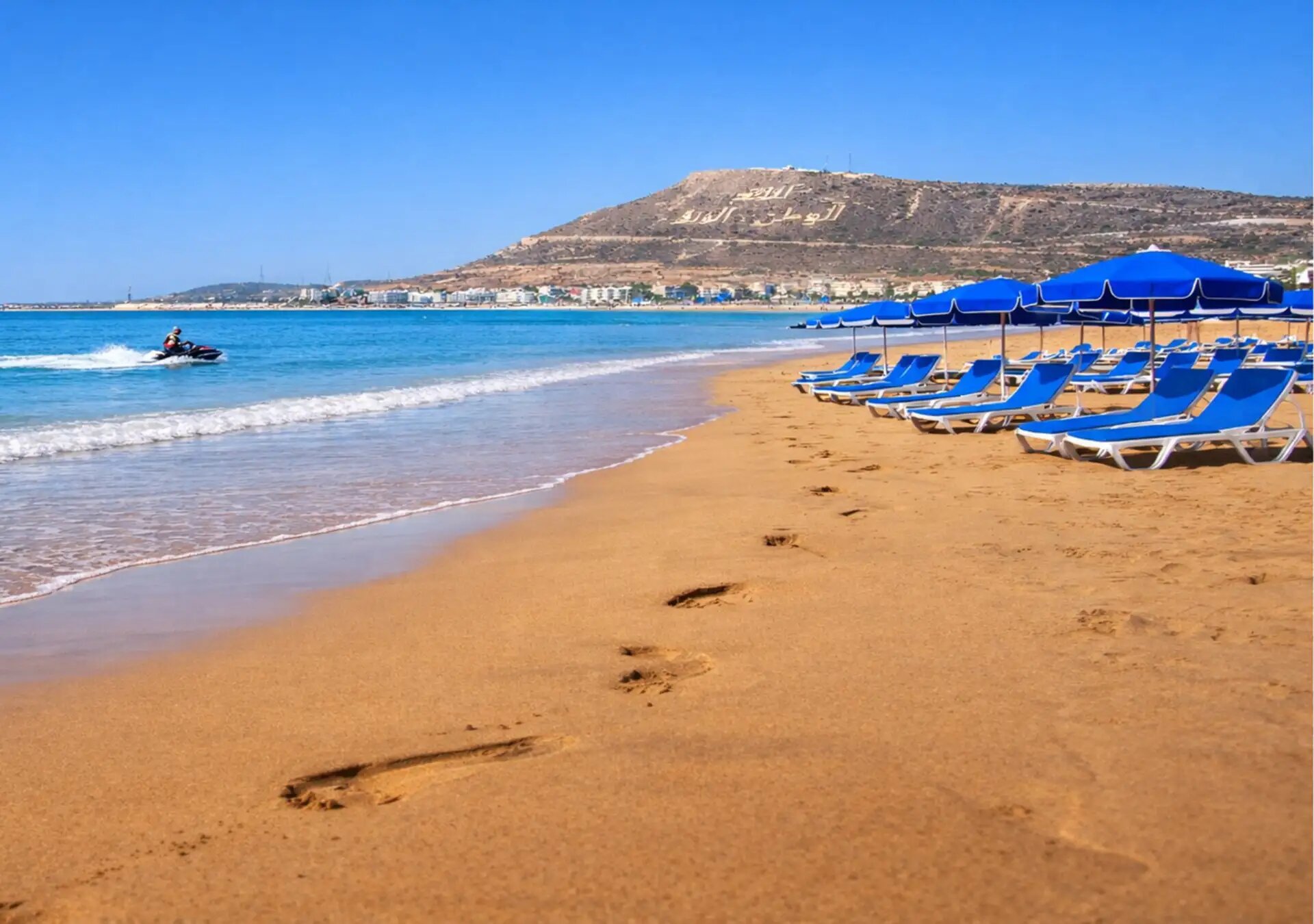 Golden sand and blue parasols on Agadir beach, with the Kasbah hill of Agadir Oufella behind