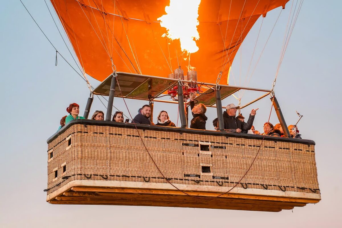 Passengers in a balloon basket under a glowing burner flame
