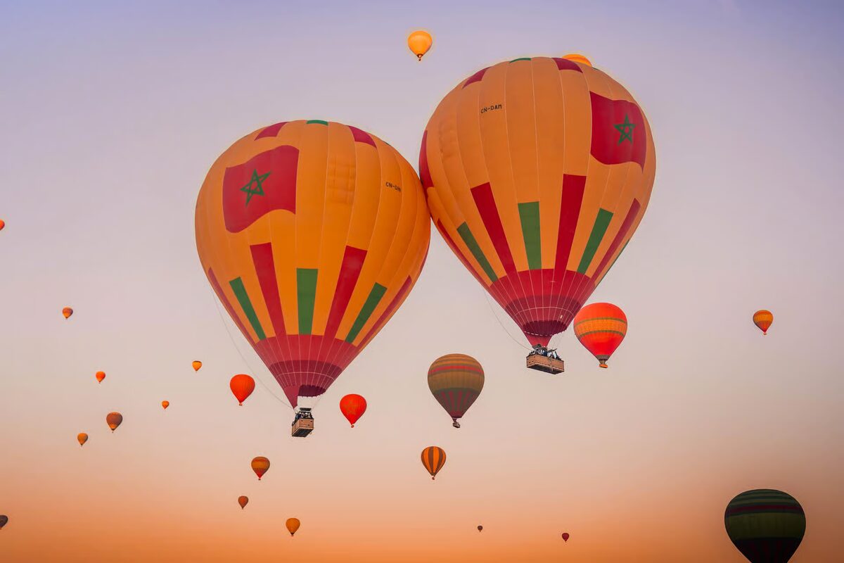 Hot-air balloons with the Moroccan flag rising into the sunrise sky over Marrakech
