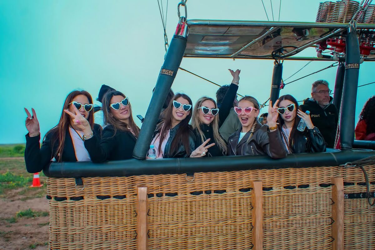 Group of friends smiling and waving from the balloon basket