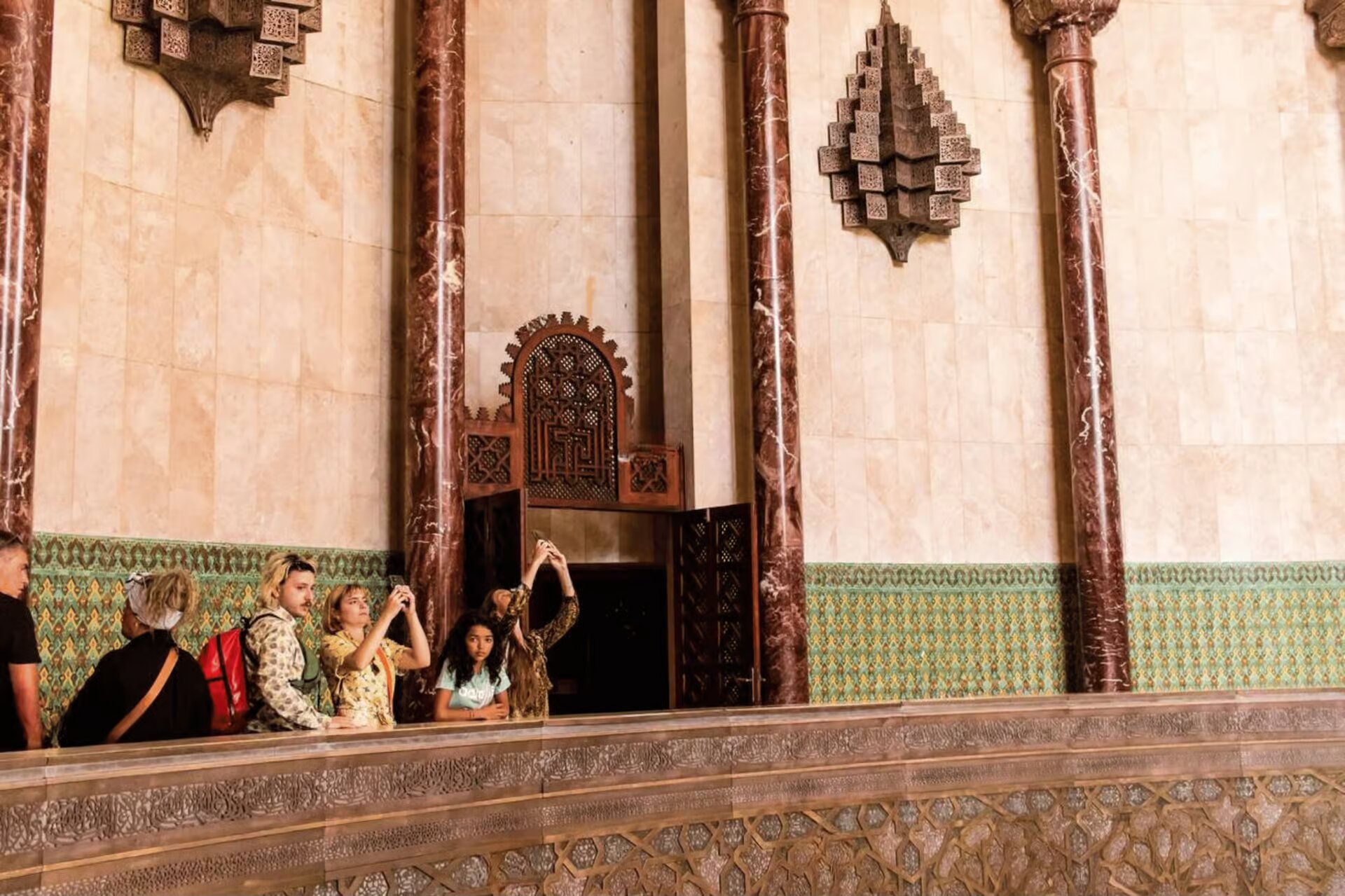 Visitors taking photos from a carved balcony inside the Hassan II Mosque