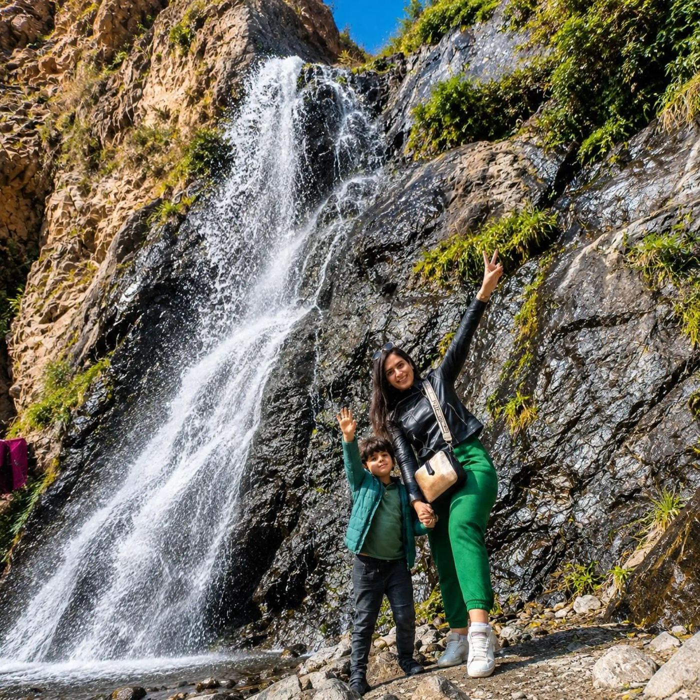 Family posing on a painted rock in front of cascading waterfalls in the Atlas Mountains