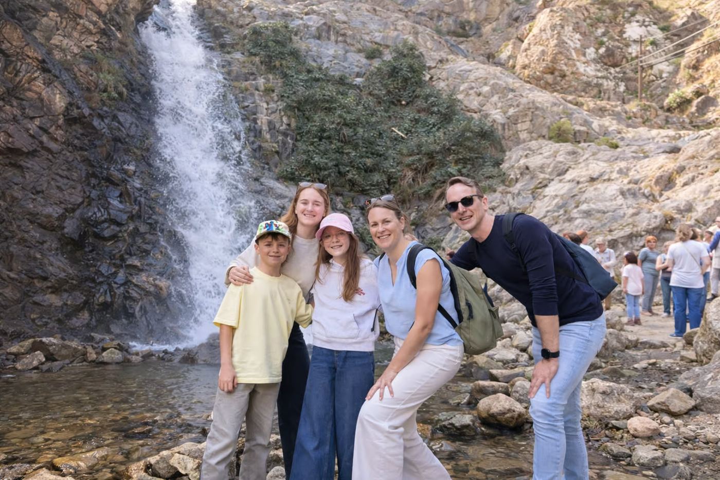Family smiling at the foot of a waterfall during the Setti Fatma hike