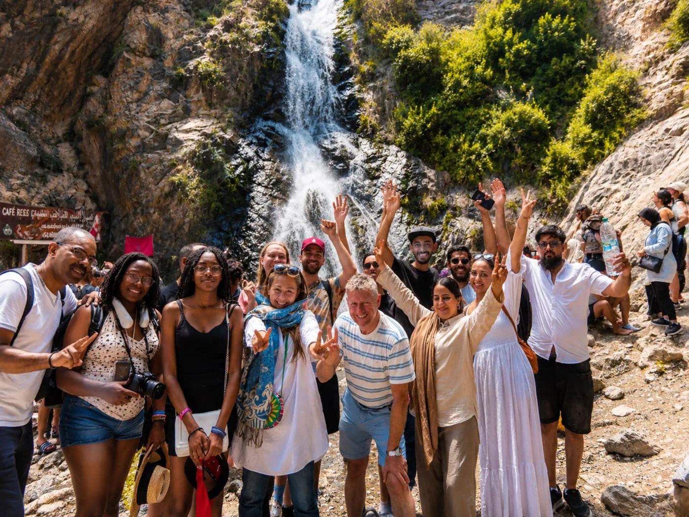 Happy group of travelers waving in front of a Setti Fatma waterfall