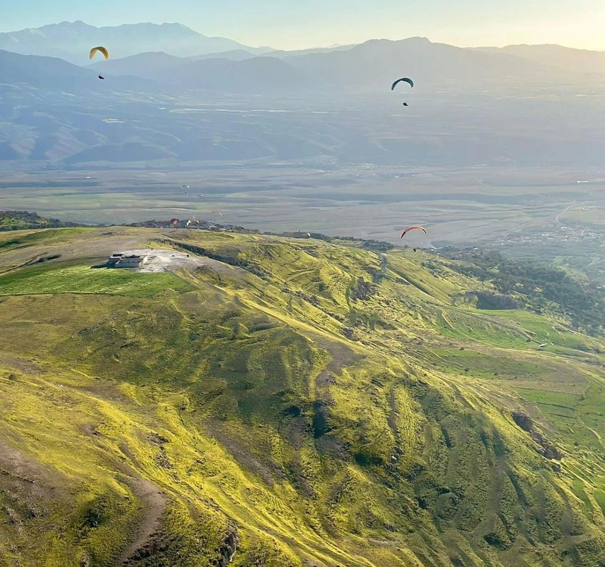 Paragliders soaring over green hills with the Atlas Mountains in the distance