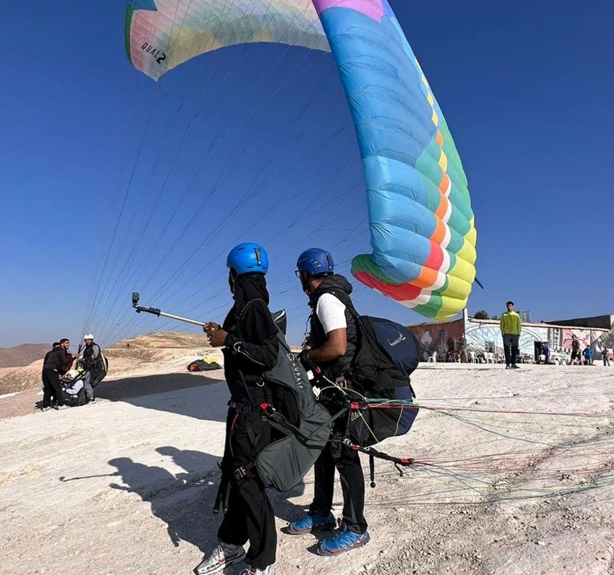Pilot and passenger preparing for take-off under a colorful paraglider wing