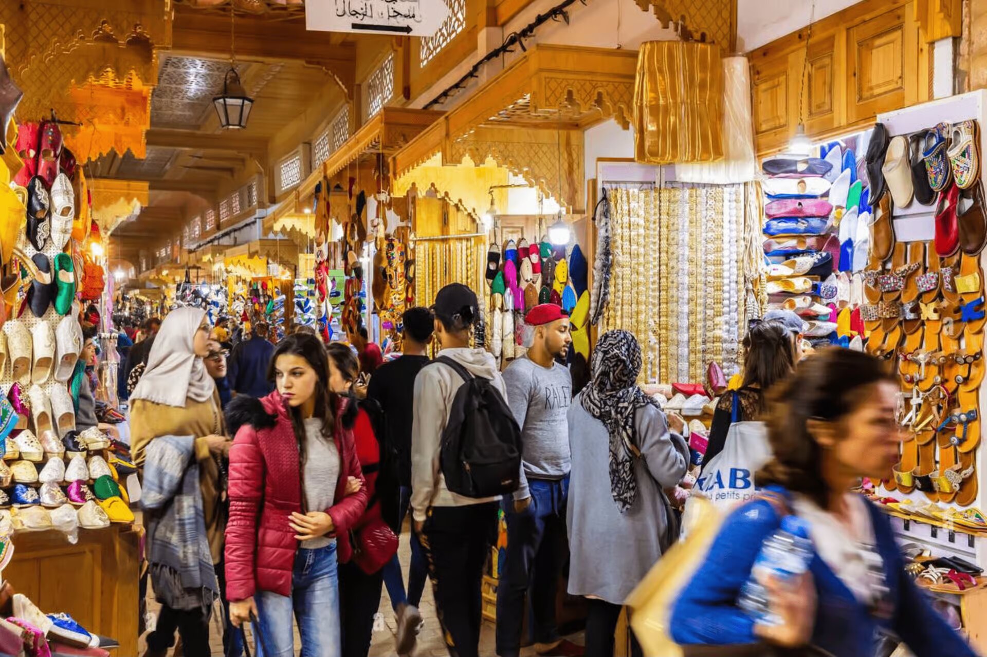Shoppers in a covered souk of the Rabat Medina lined with slippers and handicrafts